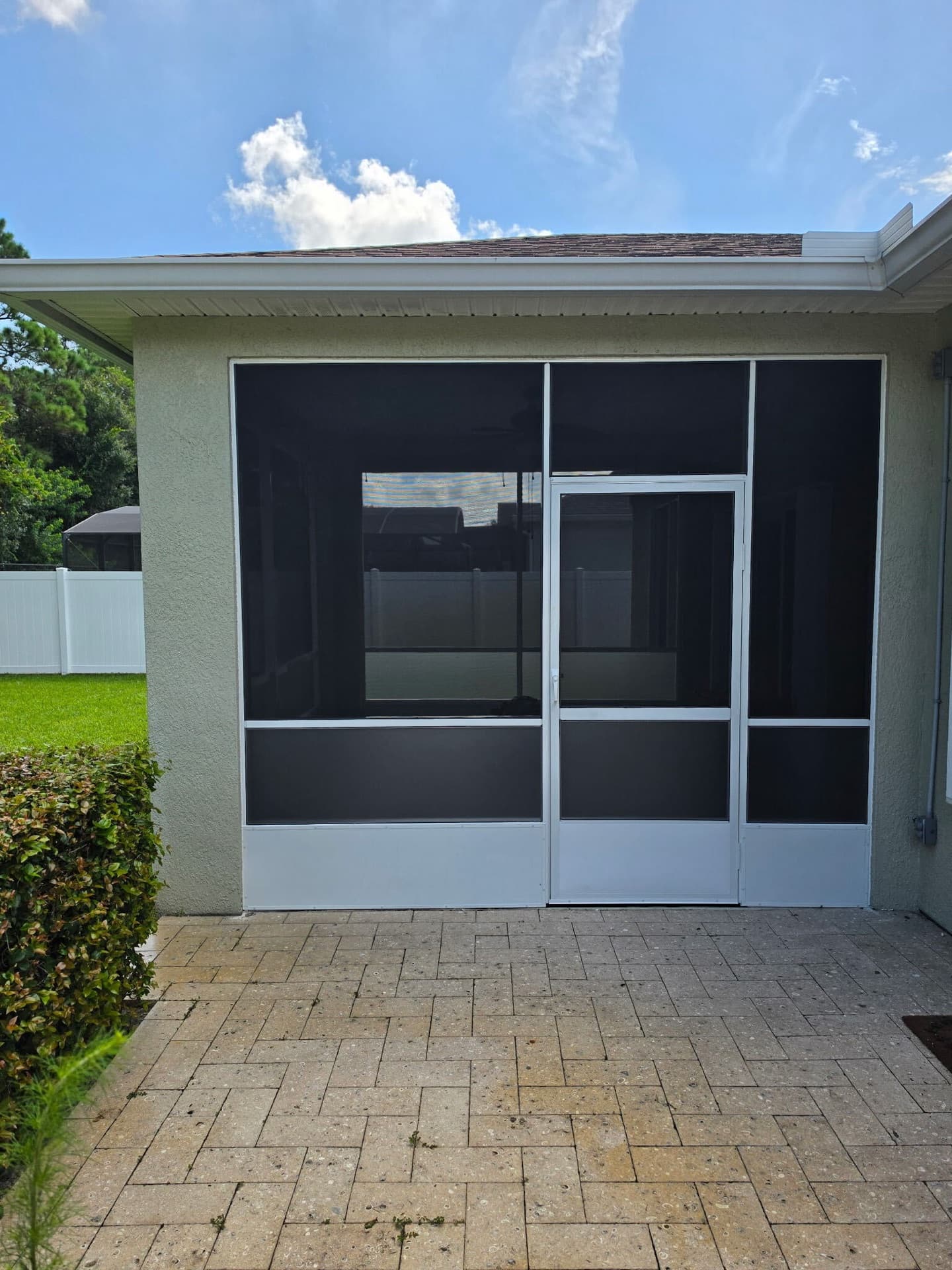 Covered patio screened in with white framing and a screen door over a paver walkway