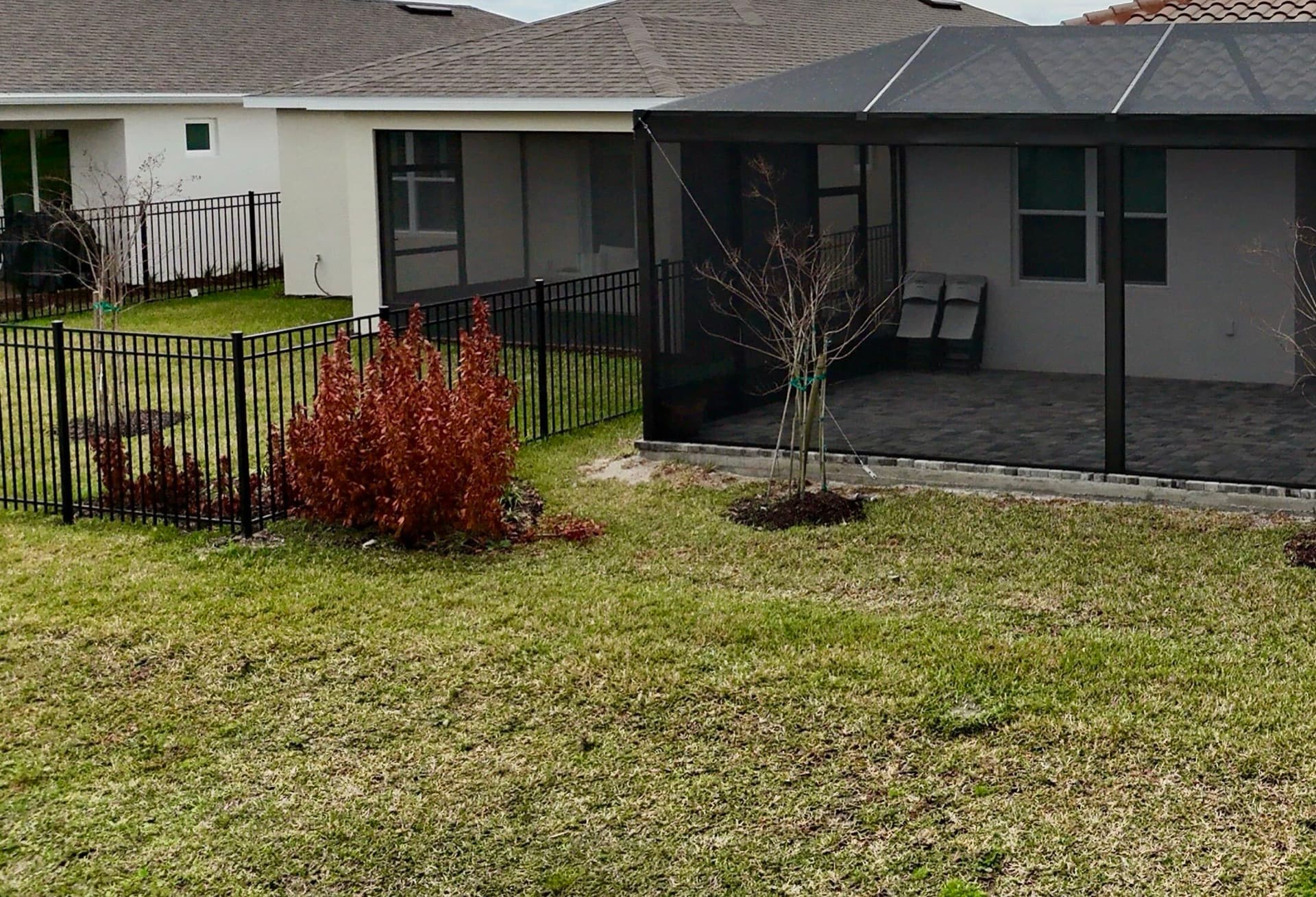Black aluminum picket fence corner with landscaping beside a screened patio