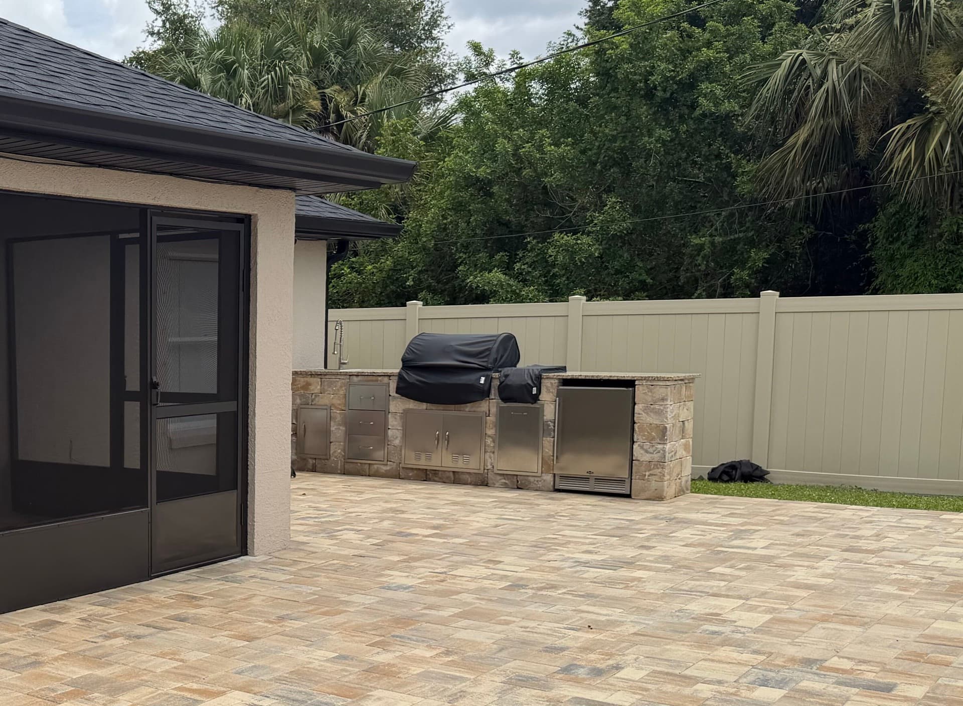 Sandstone vinyl privacy fence behind an outdoor kitchen and paver patio