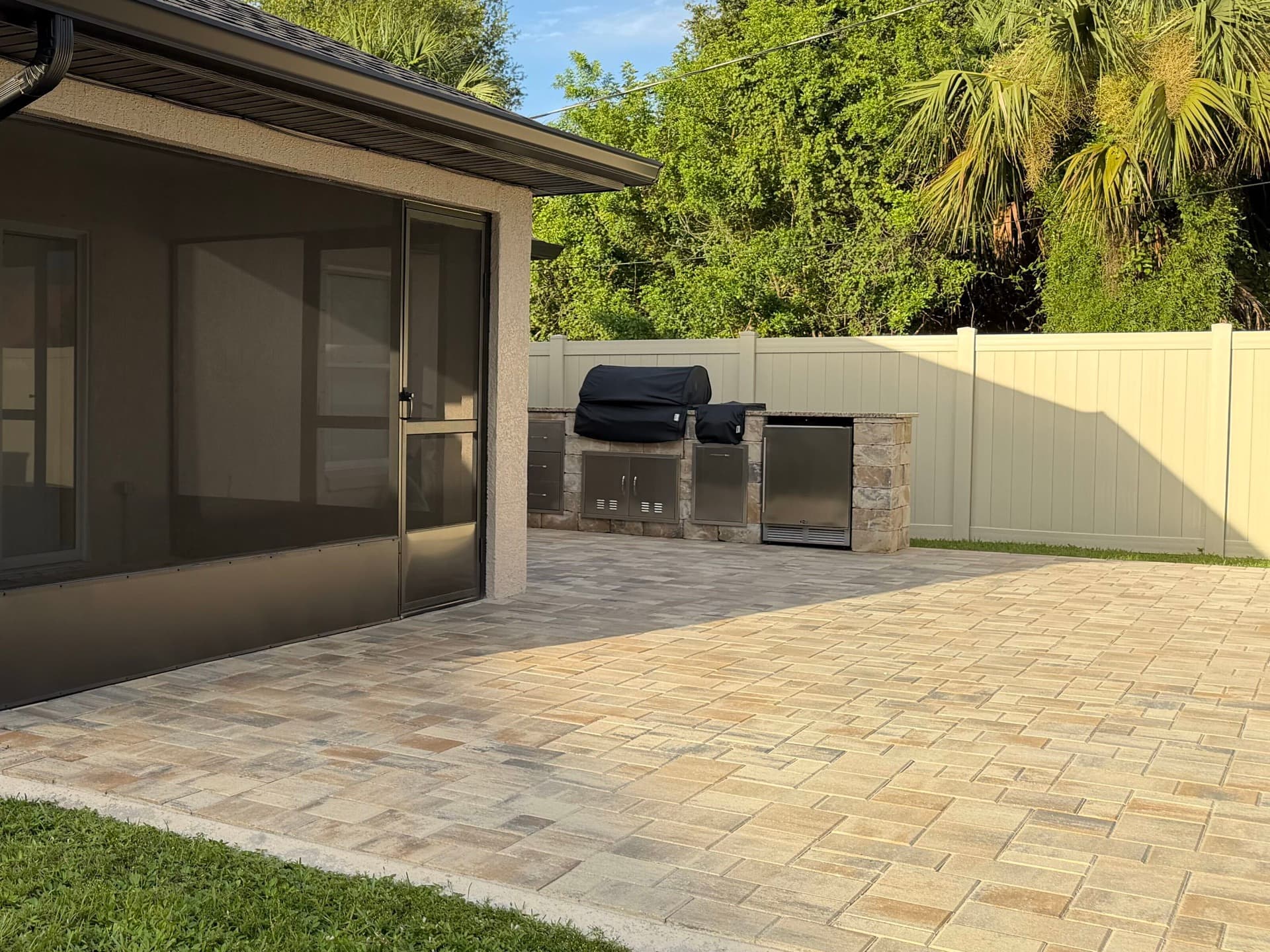 Sandstone vinyl privacy fence behind a paver patio and outdoor kitchen in Brevard County